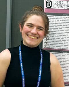 Rosalia Palumbo wearing a black shirt and lanyard in front of a bulletin board. 