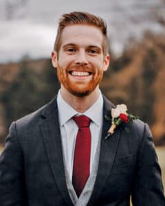 Seth Johnson wearing a suit and tie, with a floral corsage on his shoulder. 