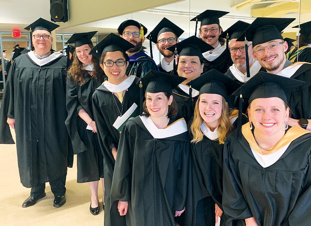 Graduates wearing caps and gowns posing together indoors for a group photo at a graduation event.
