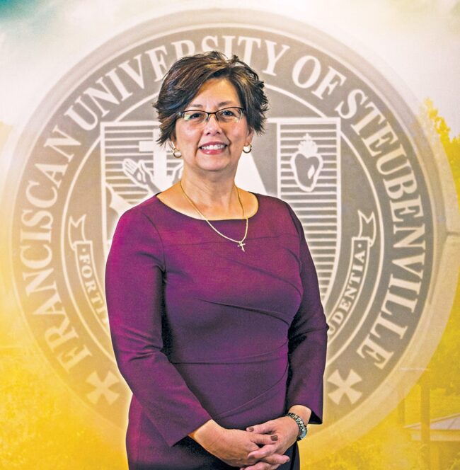 Dr. Diann Schmitt standing and posing indoors in front of a backdrop featuring the Franciscan University of Steubenville seal.