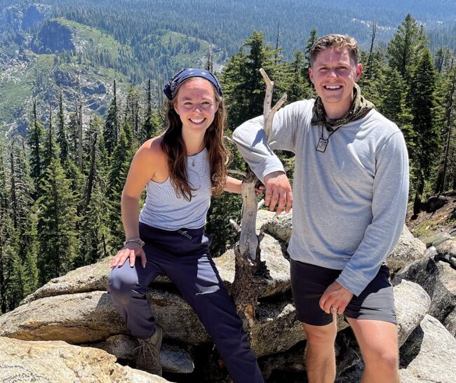 Helena (Stadnik ’19) and Michael ’20 Araps posing outdoors on rocky terrain with a forested mountain landscape in the background.