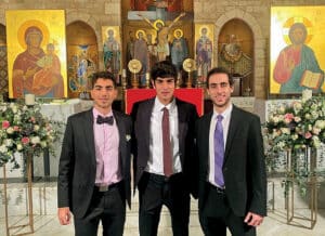 Three men dressed in suits posing together inside a church, standing in front of an altar with a crucifix and religious icons.