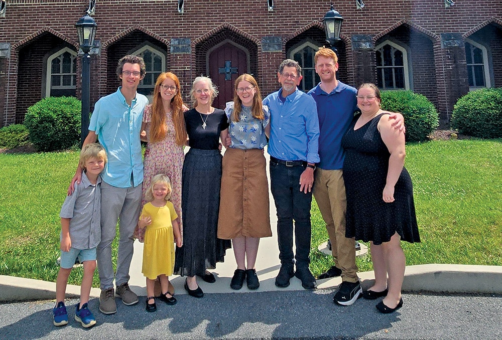 A group of adults and children standing together outdoors in front of a brick building with arched windows.