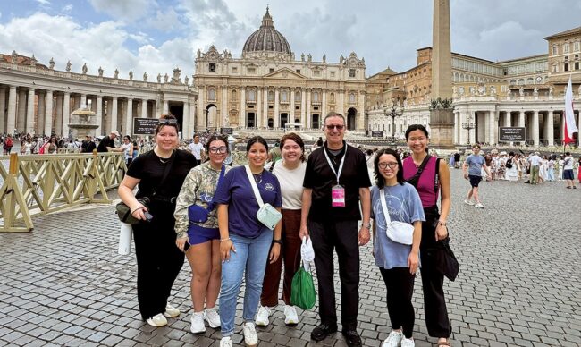 Group of pilgrims posing together in St. Peter’s Square with St. Peter’s Basilica visible behind them at the Vatican.
