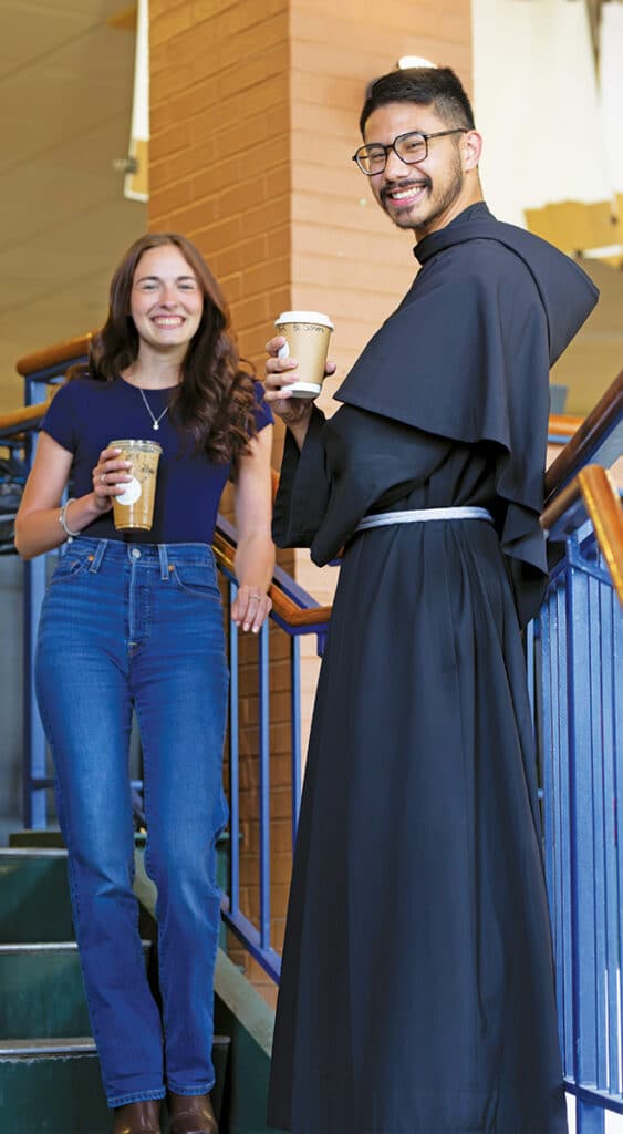 Br. Simon Mary Arellano, TOR ’22 and a student holding coffee cups while standing on a staircase indoors.