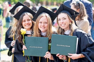 Franciscan University Class of 2026 graduates posing outdoors with diploma covers after commencement.