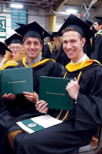 A group of graduates in cap and gown holding a Franciscan University of Steubenville diploma.