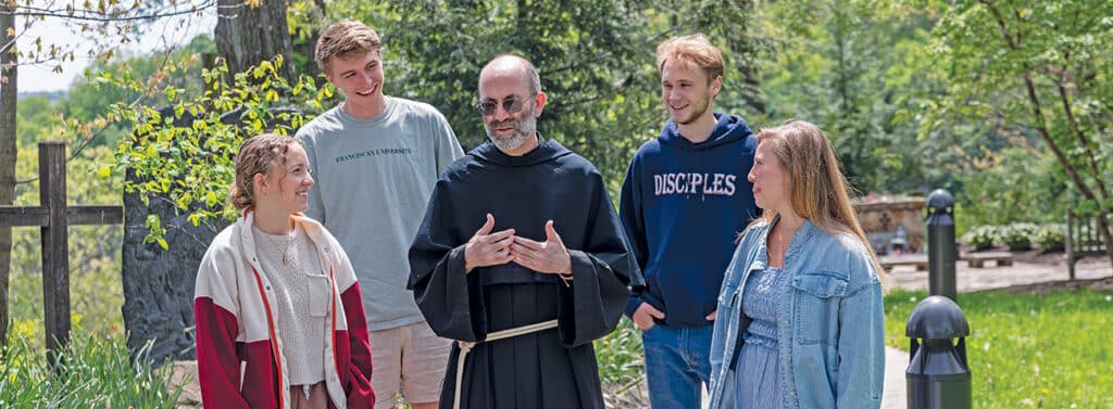 Fr. Jonathan St. Andre, TOR, speaking with Franciscan University students outdoors on campus.