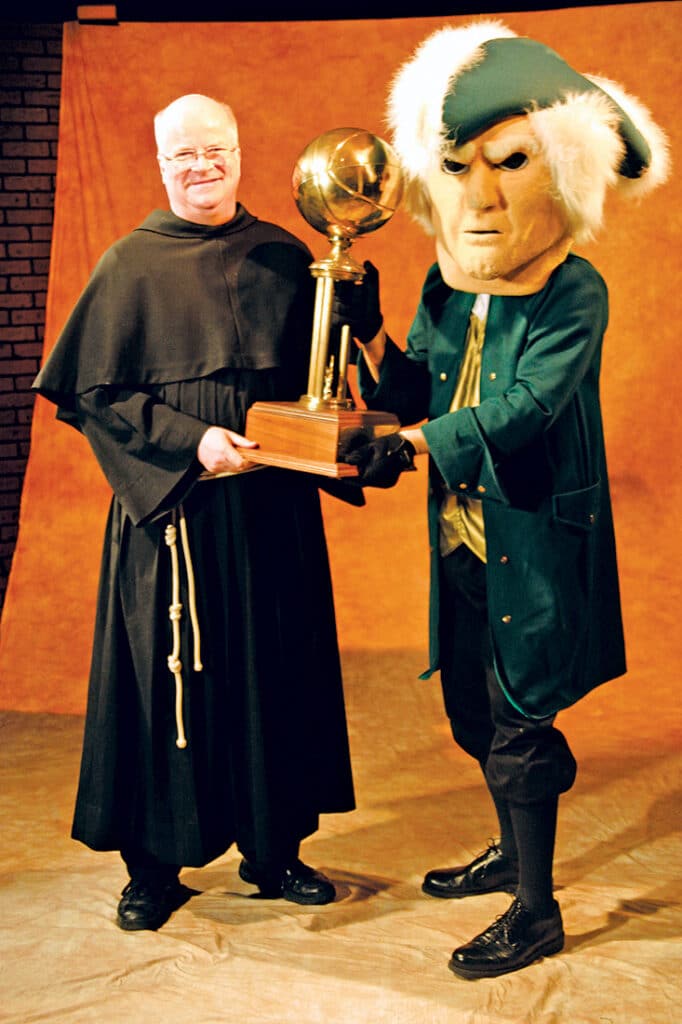 Fr. Terence Henry, TOR, and the Franciscan University mascot holding a championship trophy.