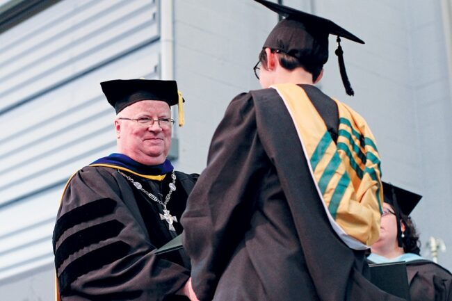 Fr. Terence Henry, TOR, presenting a diploma to a graduate during a Franciscan University commencement ceremony.