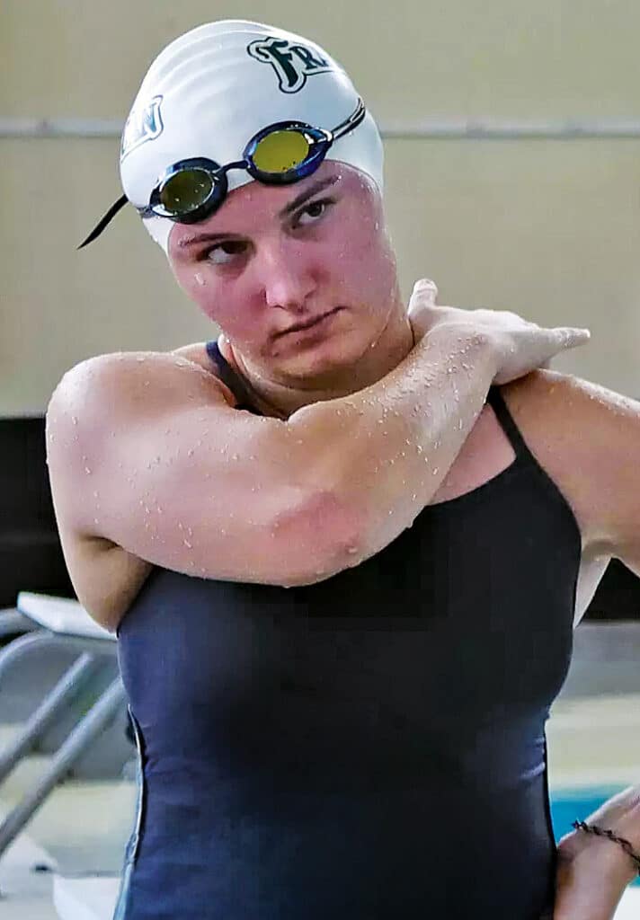 Kate Kinst stretching beside a pool while wearing a Franciscan swim cap and goggles.