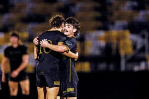 Lex Lang and Nate Bateman embracing during a rugby semifinal match under stadium lights.