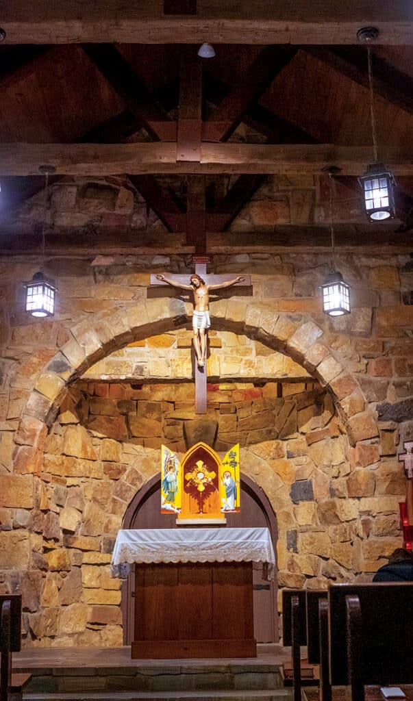 Interior of the Portiuncula Chapel featuring a stone altar, crucifix, and rustic chapel architecture.