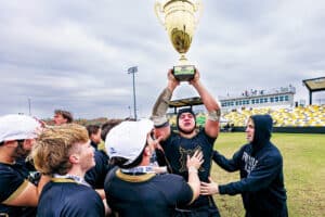 Samuel King hoisting a national championship trophy while surrounded by teammates on a rugby field.