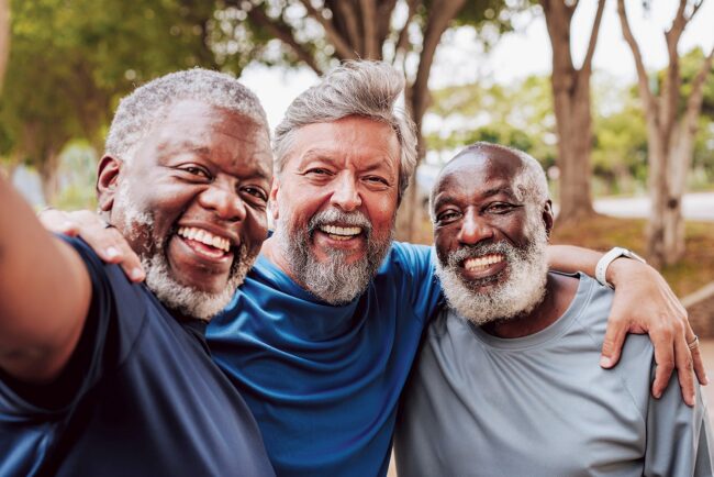 Three older men smiling together outdoors in a group selfie.