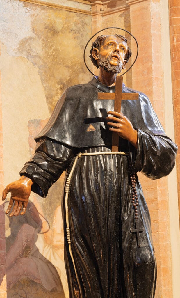 Statue of Saint Francis of Assisi holding a cross and rosary inside a Catholic church.