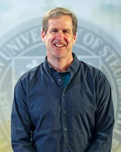 Portrait of Dr. Daniel Kuebler in front of the university seal.