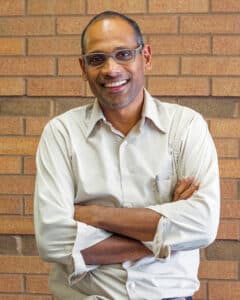 Portrait of Dr. Joseph Pathakamuri wearing glasses and standing with his arms crossed.