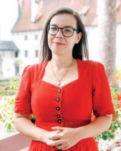 Portrait of Dr. Katarzyna Dudek wearing glasses and a red dress outdoors.