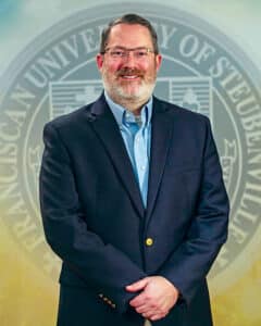 Portrait of Dr. Logan Gage in front of the university seal.