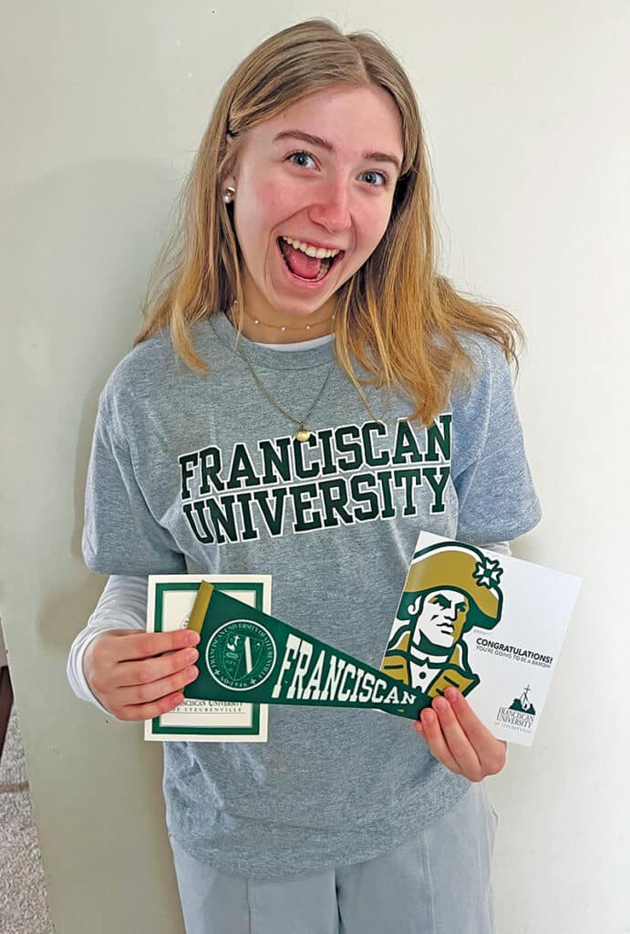 Student holding Franciscan University of Steubenville materials while wearing a Franciscan University shirt.