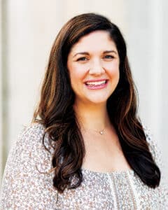Professional portrait of Katherine (Hoffer ’10) Stanek, CNM with long dark hair wearing a floral-patterned blouse.