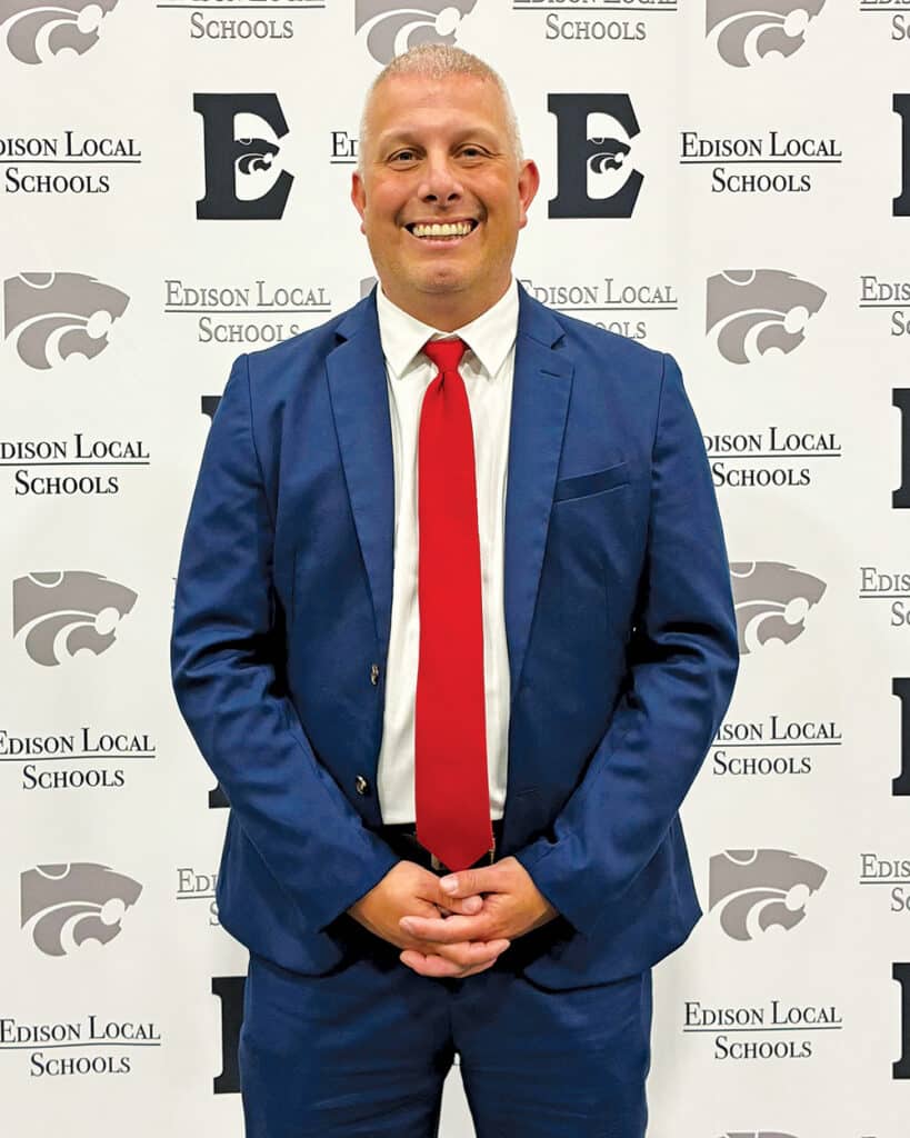 Professional portrait of Josh Leasure MSA ’11 in front of an Edison Local Schools backdrop with school logos.