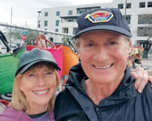 Robert Martinez and Dr. Donna Krutka posing together outdoors near a display of colorful woven bags.