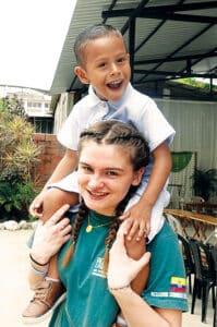 Suzanne Judge carrying a young boy on her shoulders while outdoors.